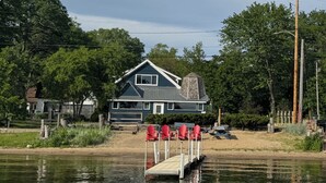 Een huis met een steiger die uitsteekt in het water, omgeven door bomen en een zandstrand.