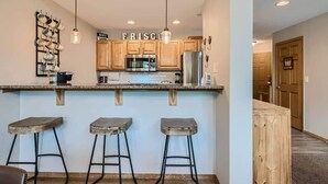 A kitchen with wooden cabinets, a stainless steel refrigerator, and a countertop with three stools. - 2 Bedroom in Tarn Landing in Frisco (Frisco)