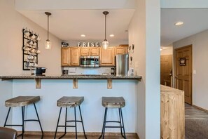 A kitchen with wooden cabinets, a stainless steel refrigerator, and a countertop with three stools. - 2 Bedroom in Tarn Landing in Frisco (Frisco)