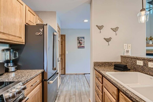 A modern kitchen with wooden cabinets, a stainless steel refrigerator, a built-in oven, and a granite countertop. - 2 Bedroom in Tarn Landing in Frisco (Frisco)