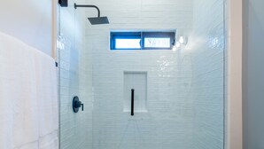 A walk-in shower with white tiled walls, a small window, and a handheld showerhead.