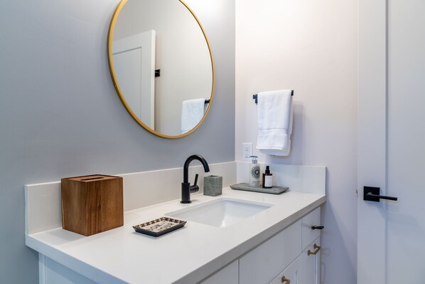 A modern bathroom with a white sink, a round mirror, and a wooden box on the counter.