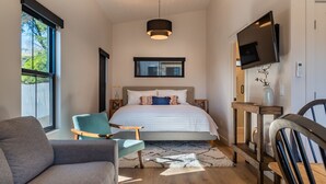 A modern bedroom with a large bed, a TV mounted on the wall, and a window providing a view of the outdoors.