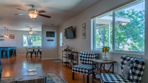 A spacious living area with a large window, a ceiling fan, and a dining area with a bar. - Vineyard Views + Gourmet Kitchen | Paso Robles CA | 46 West Walnut Hill (Paso Robles)