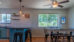 A modern kitchen with a central island, bar stools, and a dining area with a table and chairs. - Vineyard Views + Gourmet Kitchen | Paso Robles CA | 46 West Walnut Hill (Paso Robles)