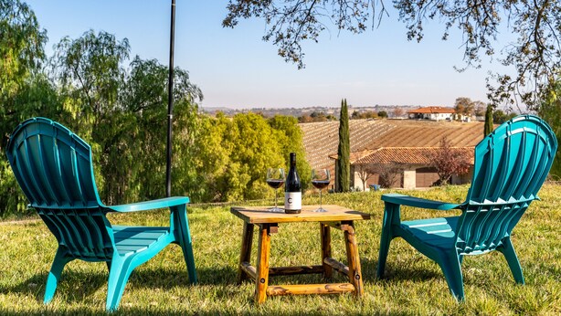 Two turquoise Adirondack chairs, a wooden table, and a bottle of wine on the grass. - Vineyard Views + Gourmet Kitchen | Paso Robles CA | 46 West Walnut Hill (Paso Robles)