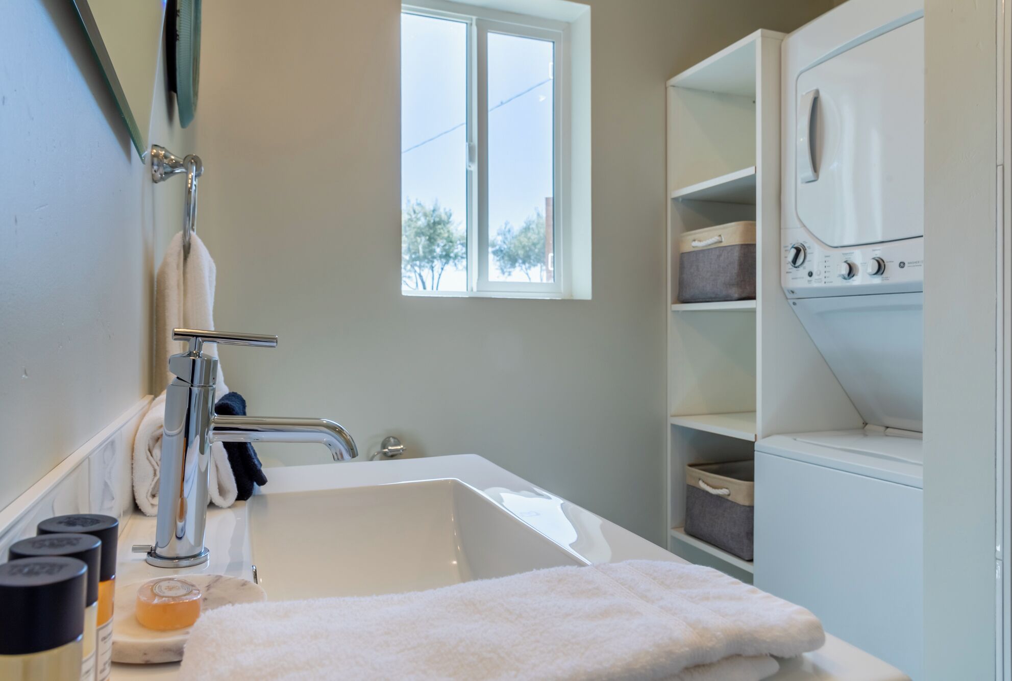 A bathroom with a bathtub, a window, a towel rack, and a laundry area.