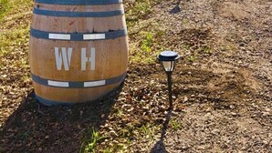 A wooden barrel with the letters "WH" on it, placed on a gravel path with a potted plant on top. - Vineyard Views + Gourmet Kitchen | Paso Robles CA | 46 West Walnut Hill (Paso Robles)
