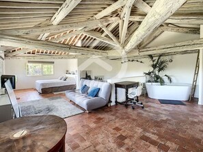 Relax in this inviting living area with a sofa, armchair, and potted plant, surrounded by a high ceiling and natural light.