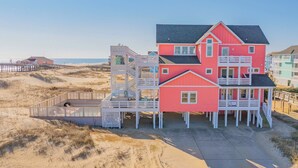 Ein mehrstöckiges Strandhaus mit roter Fassade, mehreren Balkonen und einer Holzterrasse.
