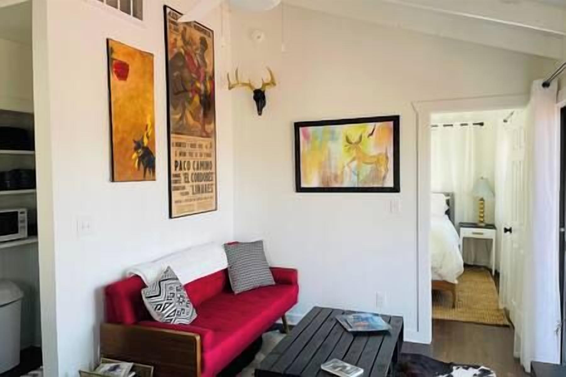 Una sala de estar con un sofá rojo, una mesa de centro y decoración en la pared que incluye un ciervo y un cartel.