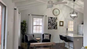 A spacious living area with a wooden bench, a dining table, and two chairs. There is a large window, a ceiling fan, and a clock on the wall. - Mountain Retreat: Virginia Foothills (Charlottesville)