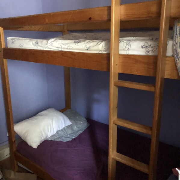 A bunk bed with a wooden frame, a purple mattress, and a white pillow.