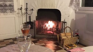 Ein gemütliches Wohnzimmer mit Kamin, einem Schachbrettmuster-Bodenbelag, einem Weinglas und einer Korb voller Bücher.