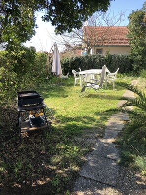A garden with a table and chairs, a gas grill, and a pathway.