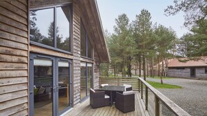 Terraza de madera con una mesa y sillas, puerta de vidrio y vista a los árboles.