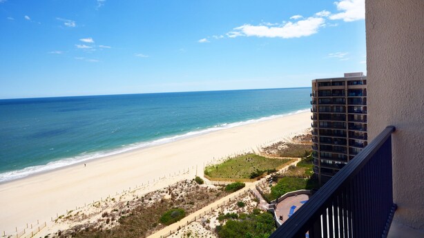 A beach view from a balcony overlooking a sandy beach and ocean. - Enjoy beautiful oceanfront views of the Ocean City coastline in this one bedroom, one bath condo located just a few steps from the beach! (Ocean City)