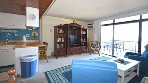 A living room with a TV, a dining area, a kitchen, and a balcony with a view. - Enjoy beautiful oceanfront views of the Ocean City coastline in this one bedroom, one bath condo located just a few steps from the beach! (Ocean City)