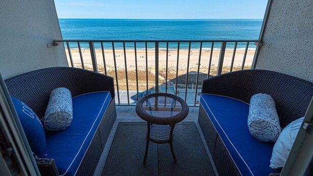 Ein Balkon mit Korbmöbeln und einem Glastisch, mit Blick auf einen Strand.