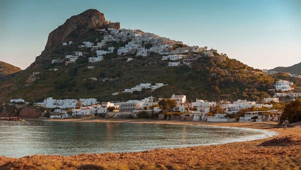 A coastal town with white buildings on a hillside, a beach in the foreground, and a rocky hill in the background. - Skyros Seaside Retreat - Serenity & Luxury Getaway (Molos)