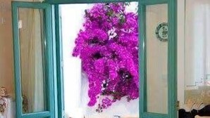 An open door leading to a dining area with a table set for two, chairs, and a view of a room with a large window and a purple flower arrangement. - Skyros Seaside Retreat - Serenity & Luxury Getaway (Molos)