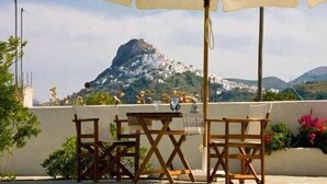 A terrace with wooden chairs and a table, overlooking a mountainous landscape with white buildings. - Skyros Seaside Retreat - Serenity & Luxury Getaway (Molos)