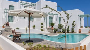A pool area with a wooden chair and umbrella, surrounded by white buildings and potted plants. - Skyros Seaside Retreat - Serenity & Luxury Getaway (Molos)
