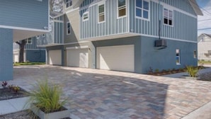 Un immeuble résidentiel à deux étages, doté d’un garage, d’une allée pavée et de petits espaces paysagers aménagés avec des plantes.