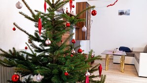A living room with a decorated Christmas tree, a clock on the wall, and a wooden ceiling. - Holiday home in the beautiful Ore Mountains (Sehmatal)