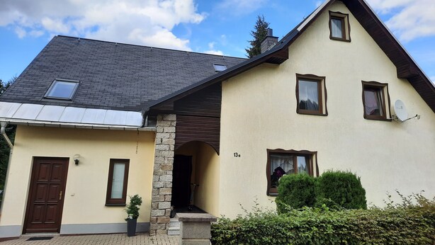 A two-story house with a sloped roof, a satellite dish, and a small garden area. - Holiday home in the beautiful Ore Mountains (Sehmatal)