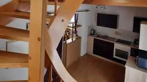 A wooden spiral staircase leading to an upper floor, a kitchen with modern appliances, and a skylight above. - Holiday home in the beautiful Ore Mountains (Sehmatal)