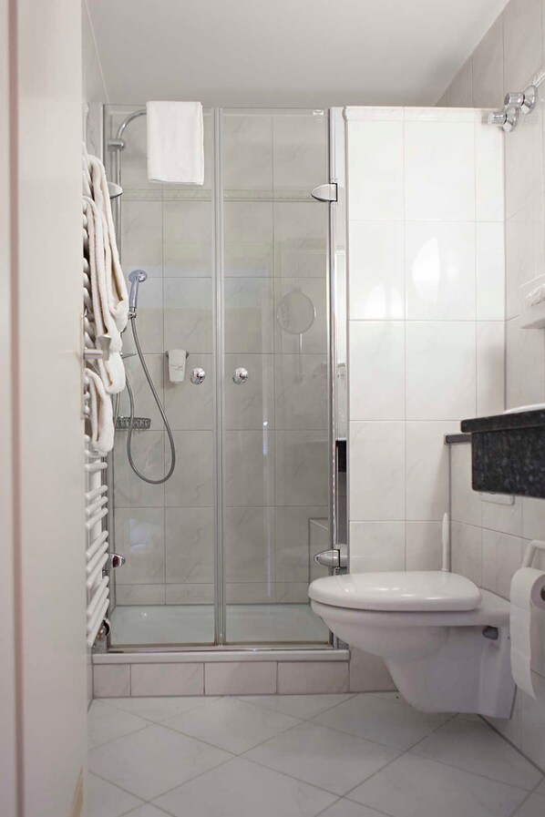 A modern bathroom with a glass-enclosed shower, white tiles, a toilet, and a towel rack.