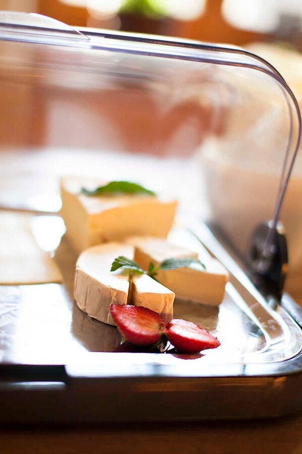 A cheese display with a glass cover, including a wheel of cheese and slices of cheese with strawberries.