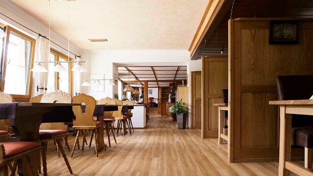 Een ruime kamer met houten vloeren, een lange tafel met stoelen en een groot raam dat natuurlijk licht binnenlaat.
