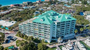 Un hotel de varios pisos con techo verde, situado cerca de un puerto deportivo con barcos amarrados.