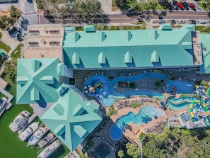 An aerial view of a resort with a large swimming pool, multiple water slides, and a parking area with several cars.