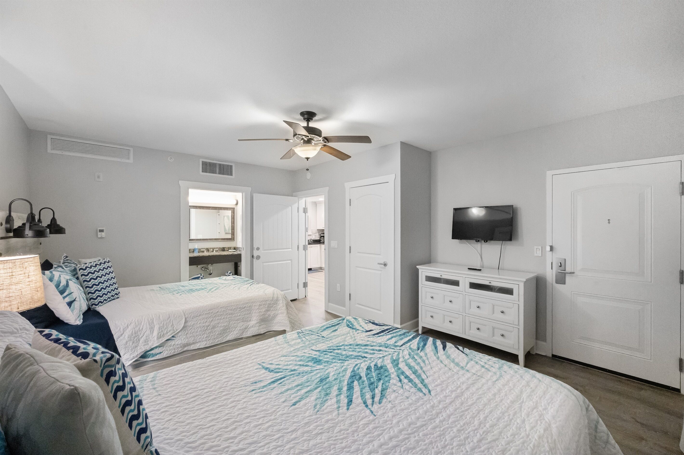 A bedroom with two beds, a ceiling fan, a TV, and a dresser.