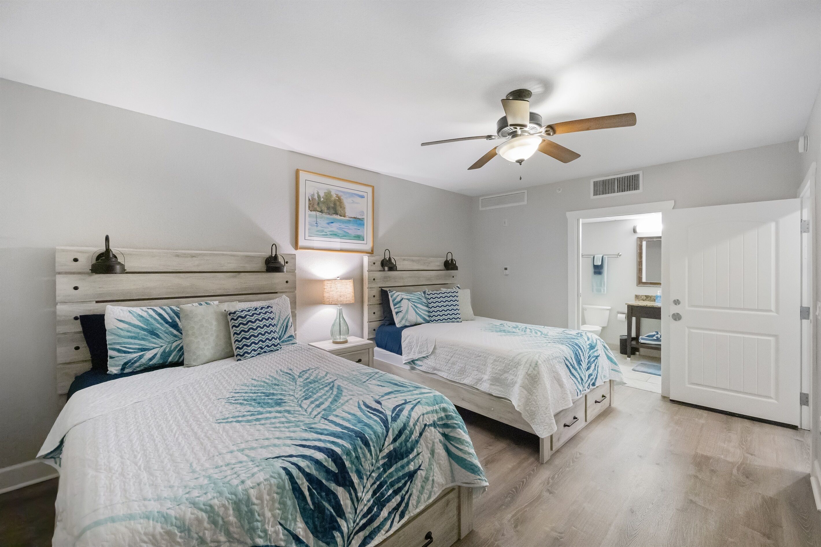 A bedroom with two beds, a ceiling fan, a nightstand with a lamp, and a framed picture on the wall.