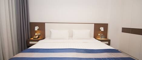 A hotel room with a large bed, two bedside tables with lamps, a wooden headboard, and a curtain on the left.