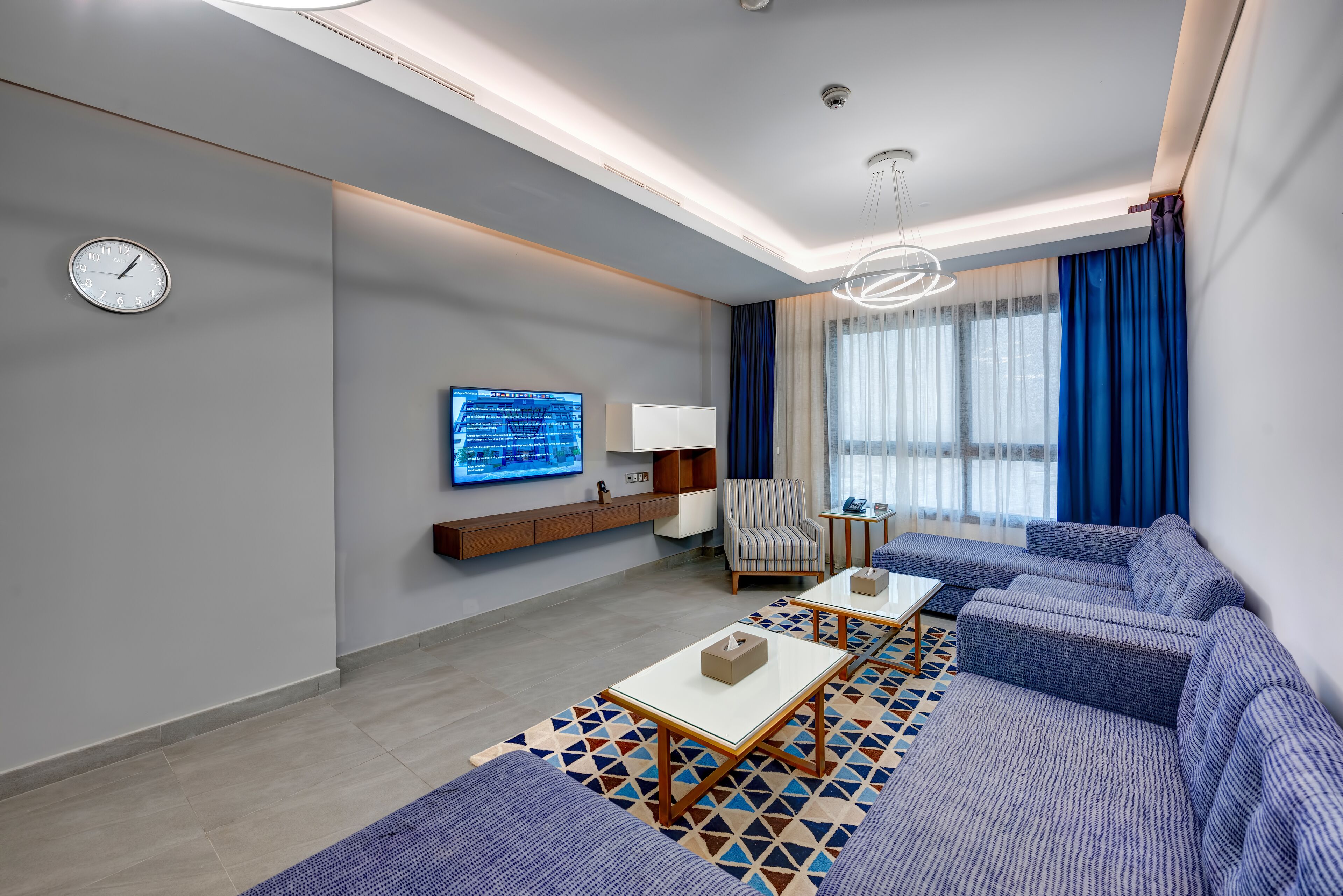 A modern living room with a sectional sofa, a coffee table, a TV mounted on the wall, and a patterned rug.