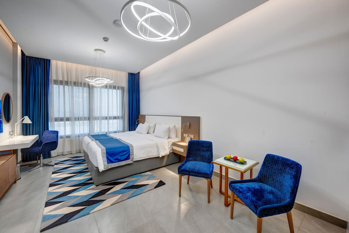 A modern hotel room with a bed, desk, chairs, and a small table with fruits.