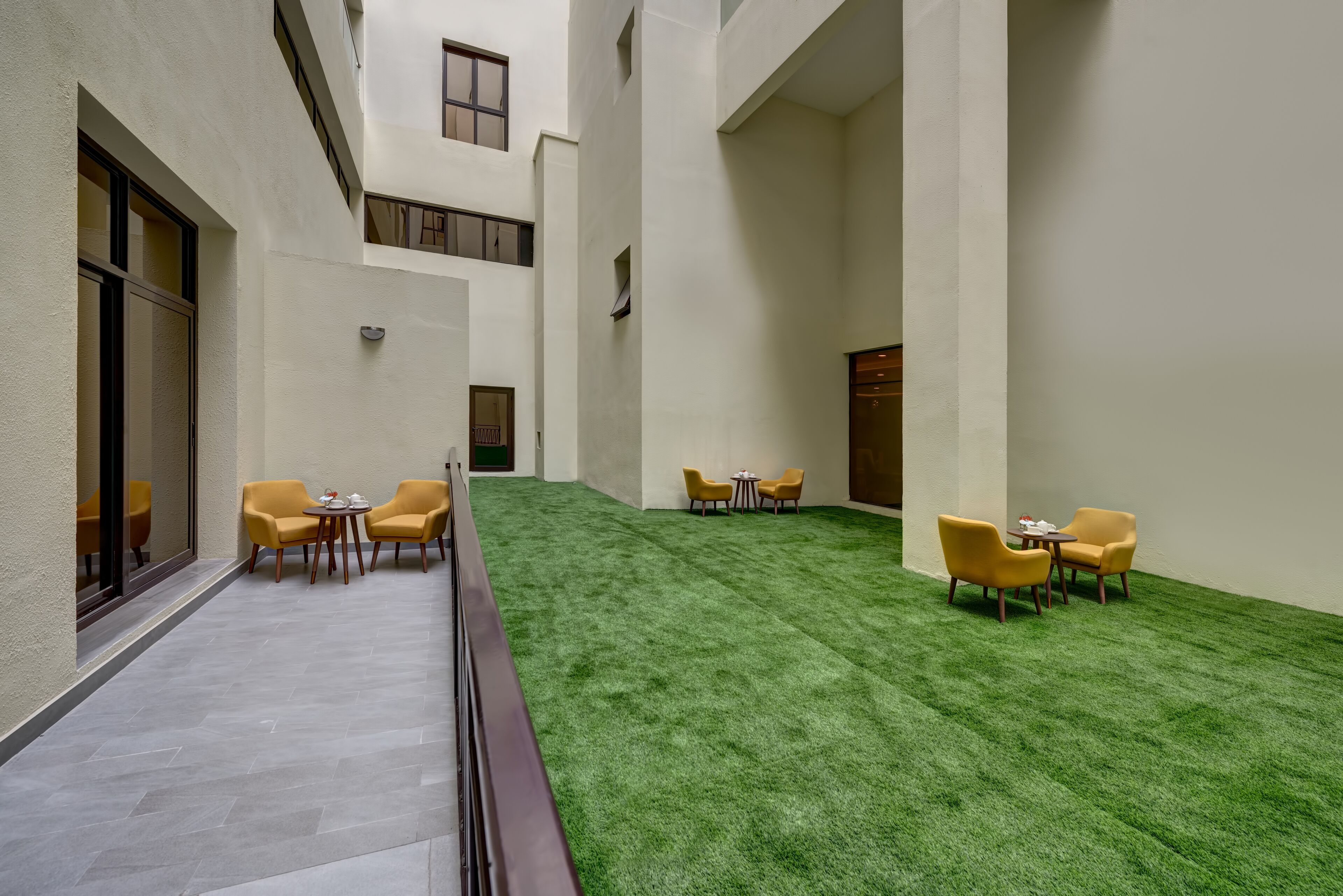 Un cortile interno moderno con erba sintetica, sedie e tavoli gialli disposti per ospitare persone.