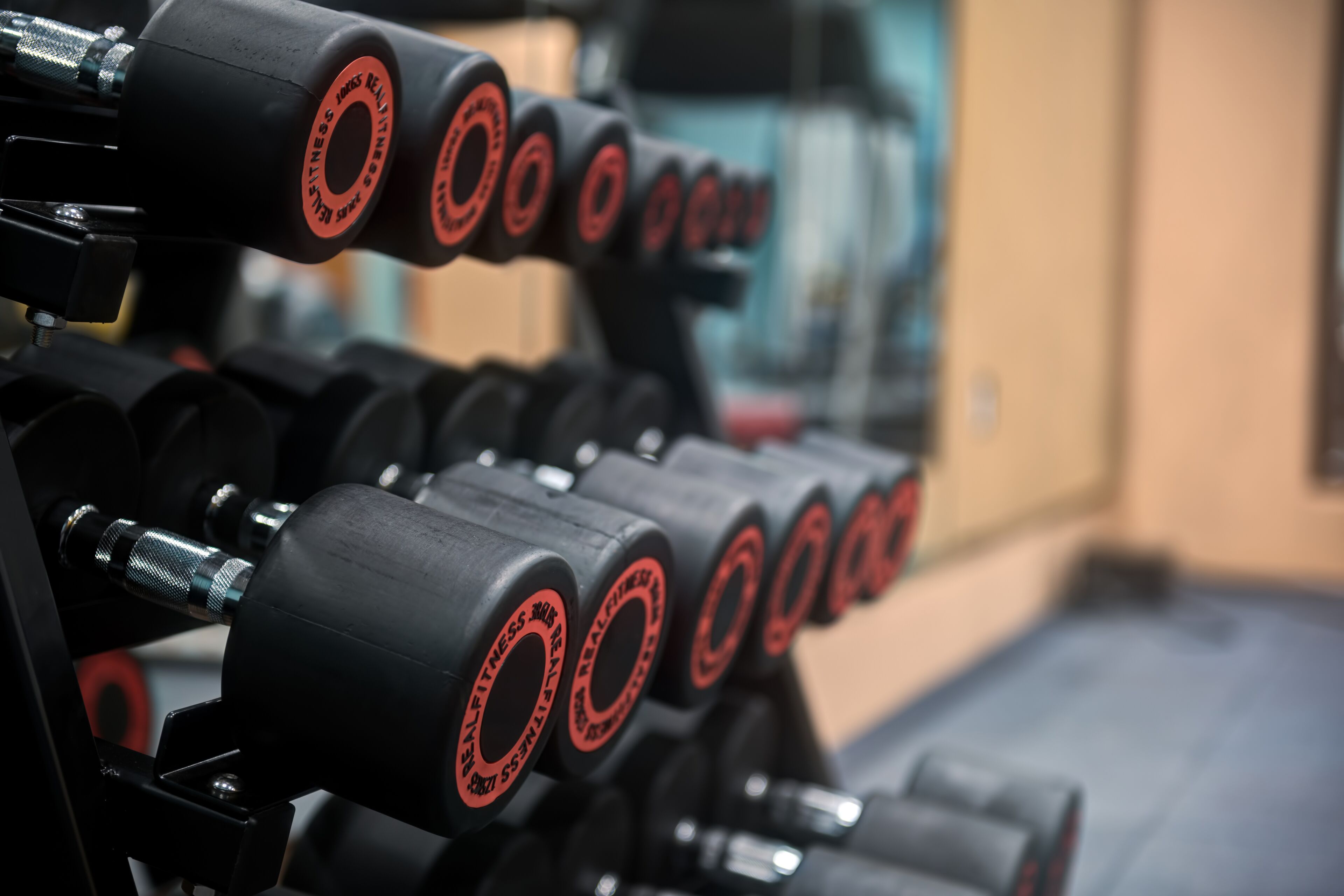 A row of black dumbbells with red text on a rack.
