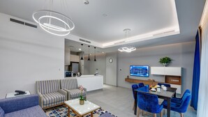 A modern living room with a sofa, coffee table, and blue chairs. There is a dining area with a table and chairs, and a kitchen in the background. - Abar Hotel Apartments (Dubai)