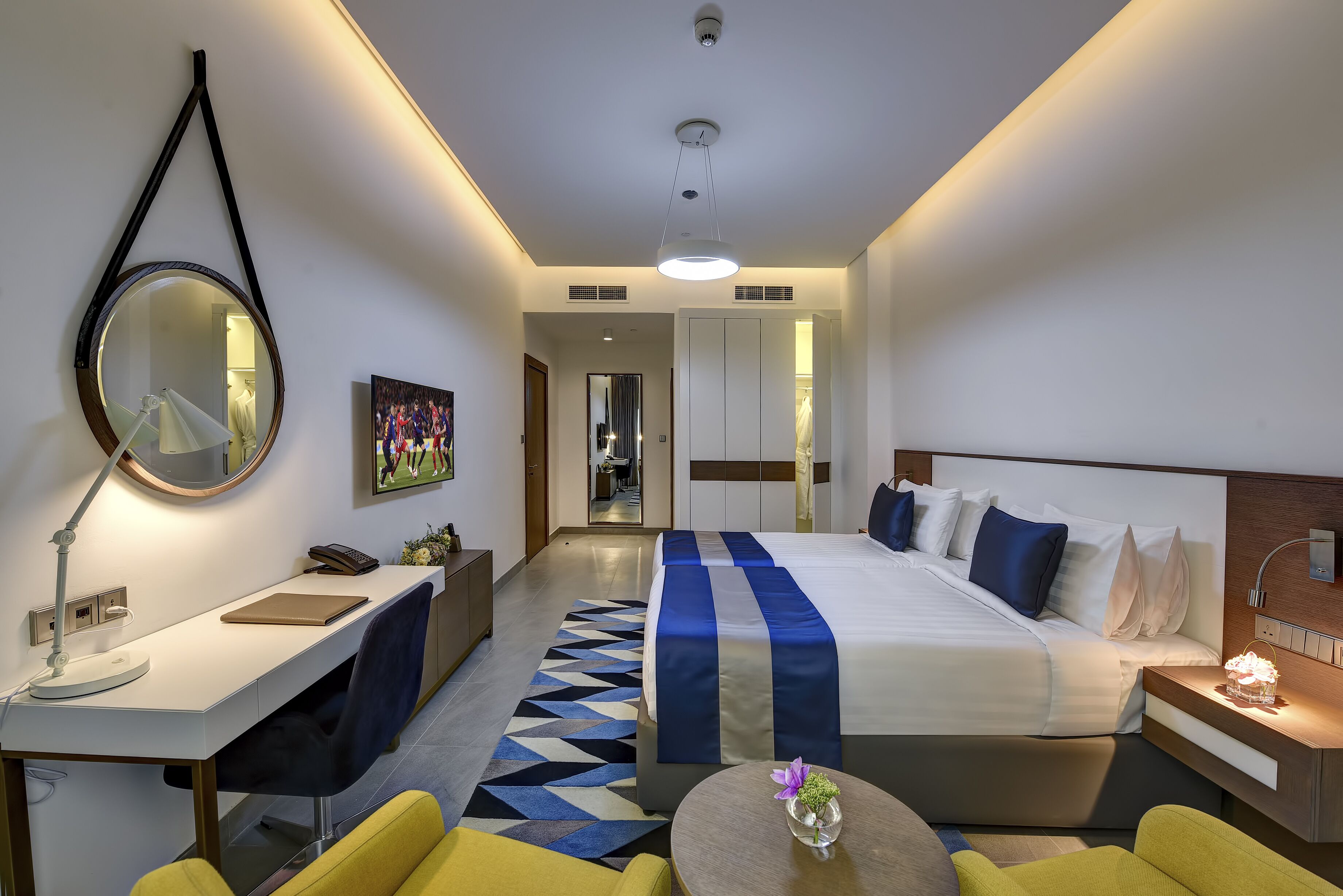 A modern hotel room with a bed, desk, chair, and a round table.