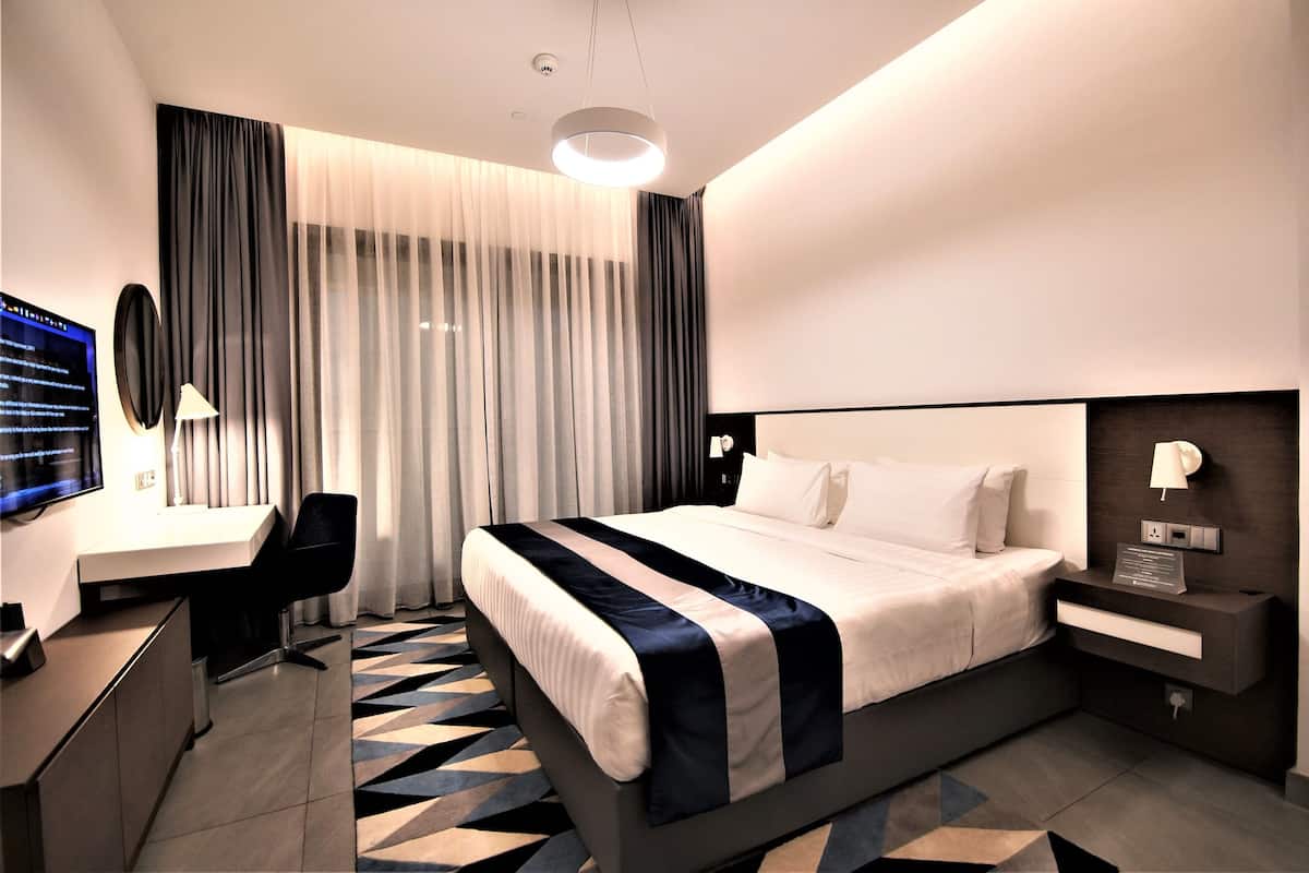 A modern hotel room with a bed, desk, chair, and a large window with curtains.