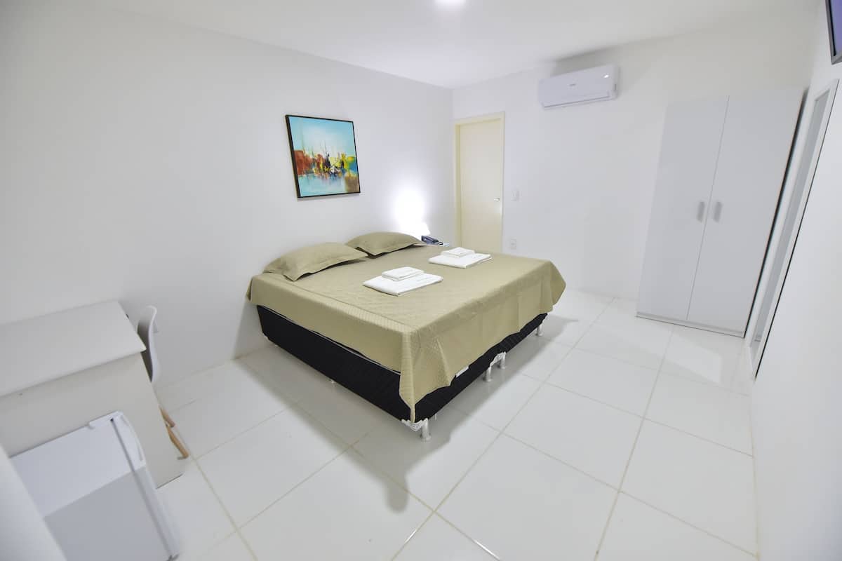 A clean, white room with a bed, a wardrobe, and a painting on the wall.