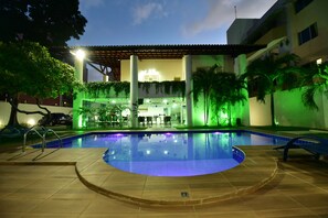 A swimming pool with a tiled deck, surrounded by palm trees and a building with a covered patio area. - Live In Fortaleza Hotel (Fortaleza)