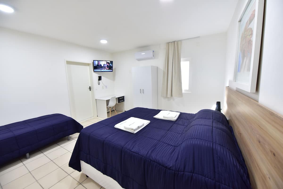 A hotel room with two beds, a TV, a desk, and a bathroom.