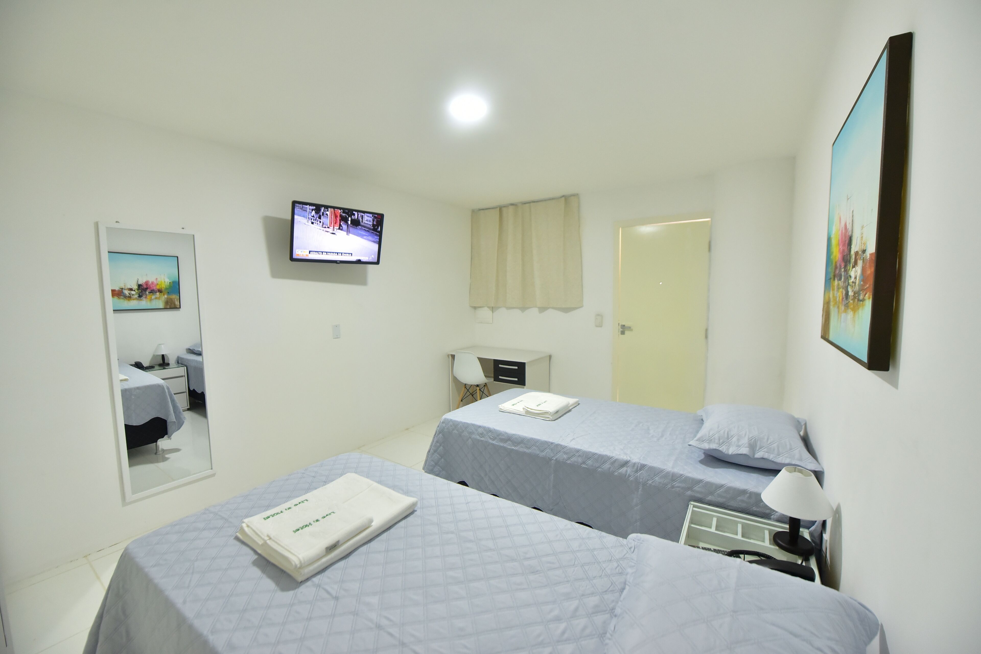 A hotel room with two beds, a TV, a mirror, and a door.